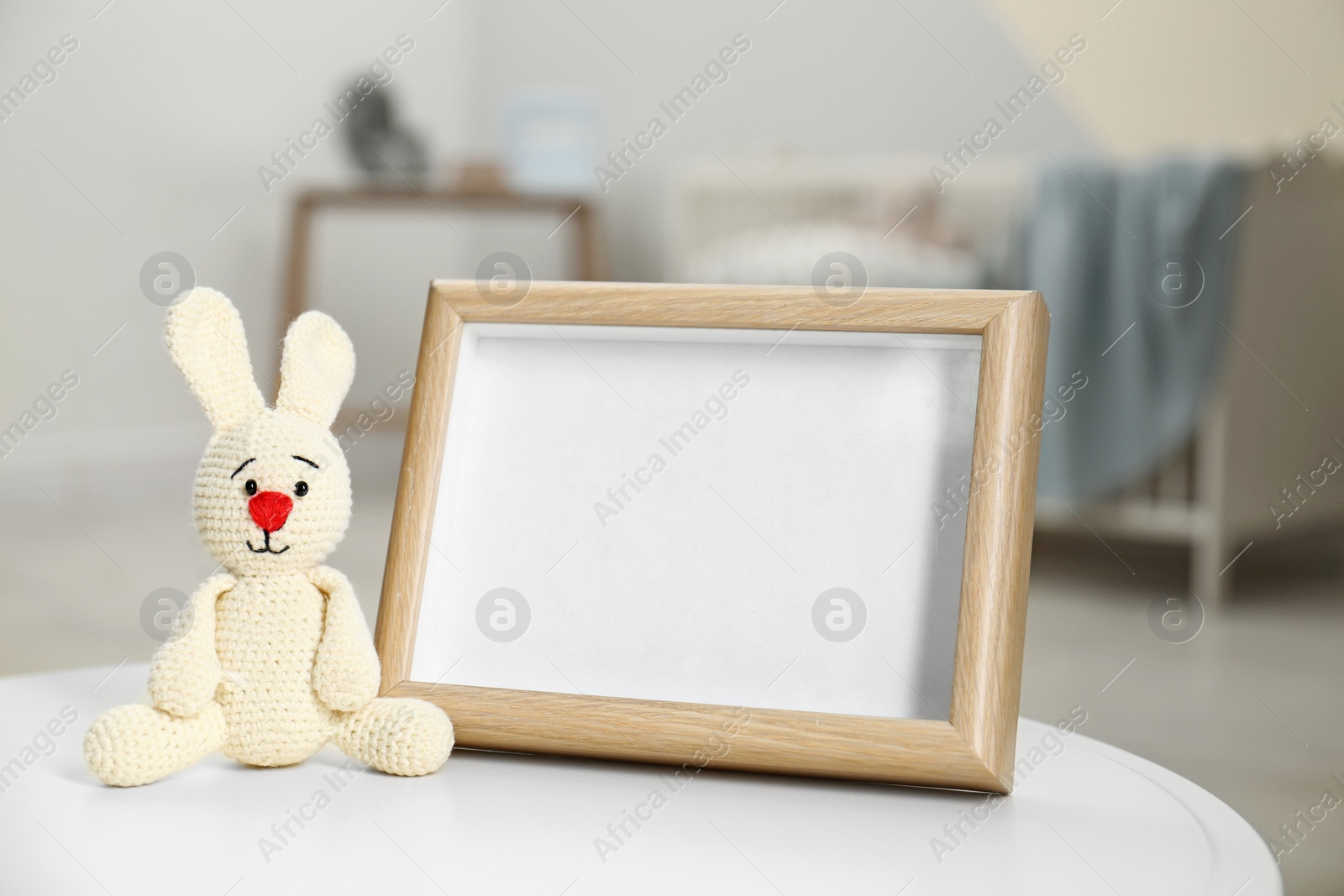 Photo of Photo frame and toy bunny on table in baby room interior. Space for text