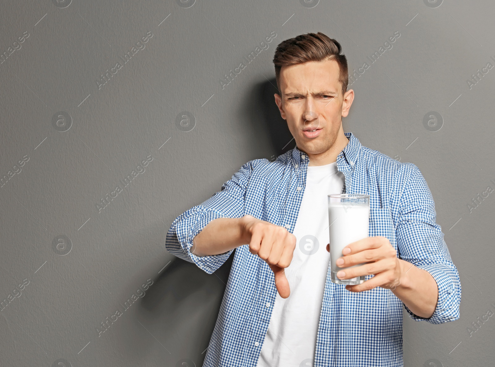 Photo of Young man with dairy allergy holding glass of milk on grey background