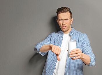Photo of Young man with dairy allergy holding glass of milk on grey background