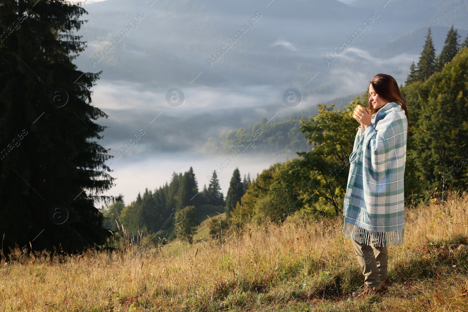 Photo of Woman with cozy plaid enjoying cup of hot beverage in nature