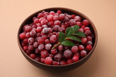 Photo of Frozen red cranberries and green leaves on beige background, closeup