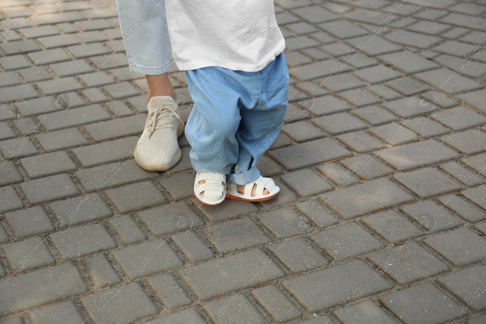 Photo of Mother supporting daughter while she learning to walk outdoors, closeup. Space for text