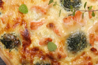 Photo of Delicious homemade quiche with salmon and broccoli as background, top view