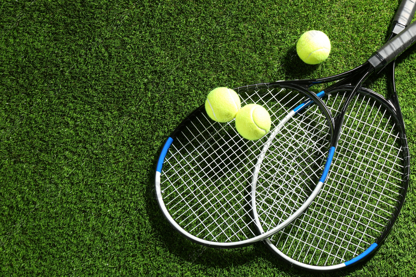 Photo of Tennis rackets and balls on green grass, flat lay. Space for text