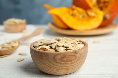 Photo of Bowl of raw pumpkin seeds on white wooden table