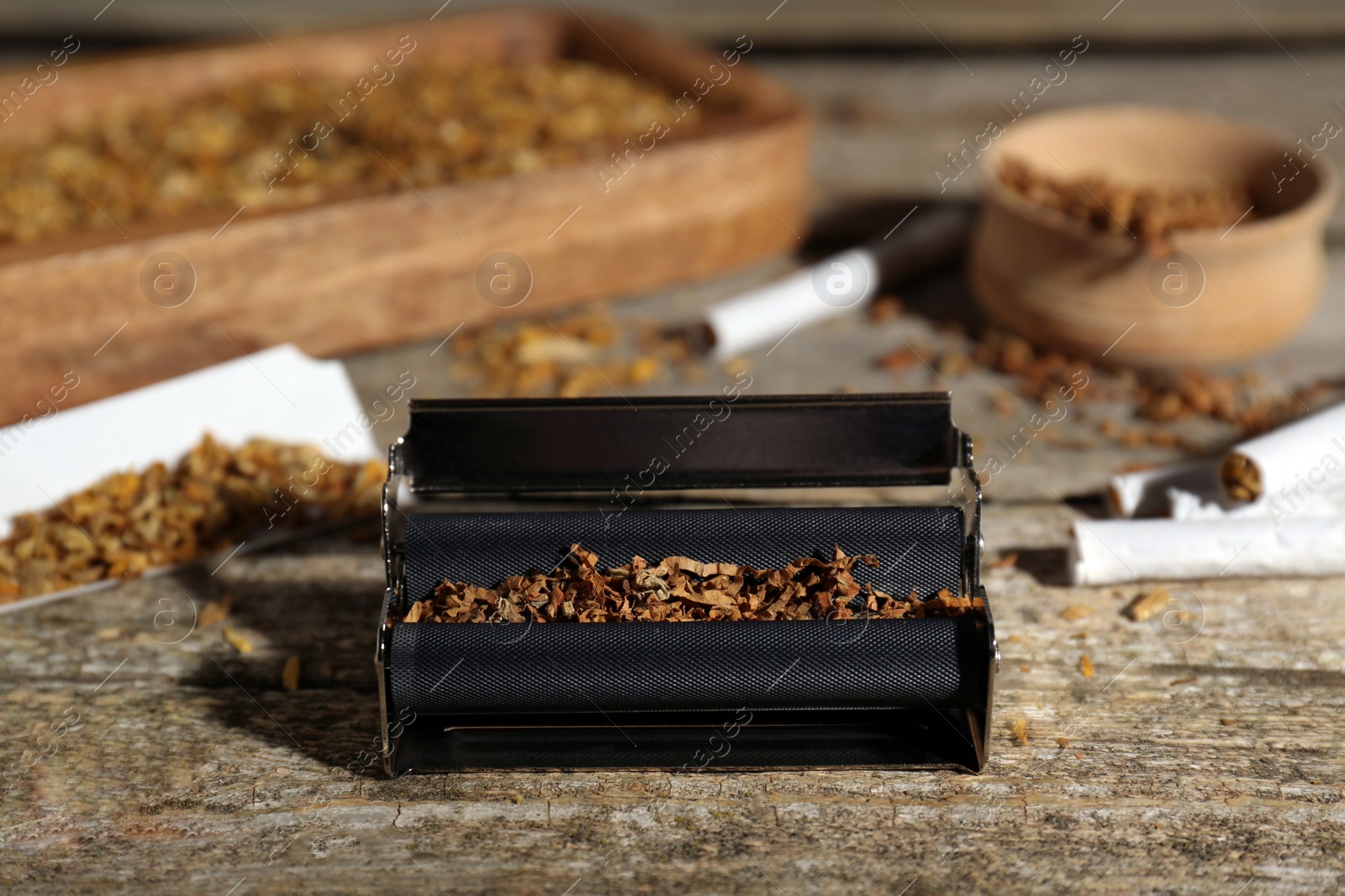 Photo of Roller with tobacco on old wooden table. Making hand rolled cigarettes