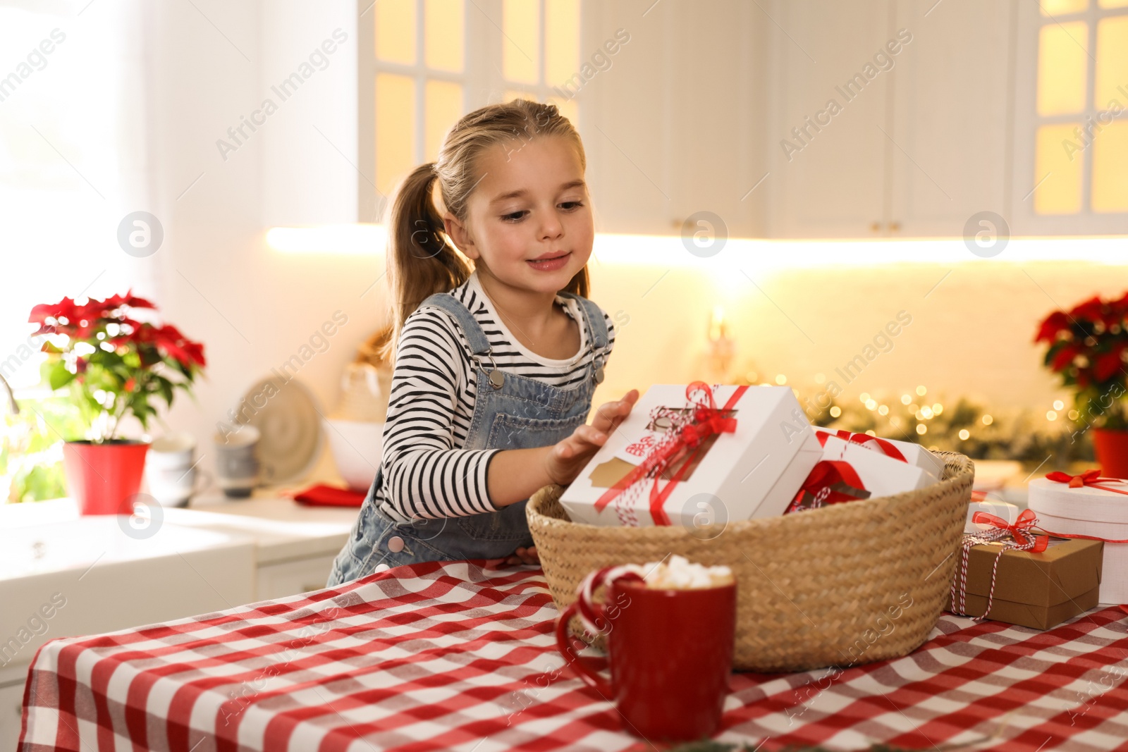 Photo of Cute little girl taking gift from Christmas advent calendar at table in kitchen