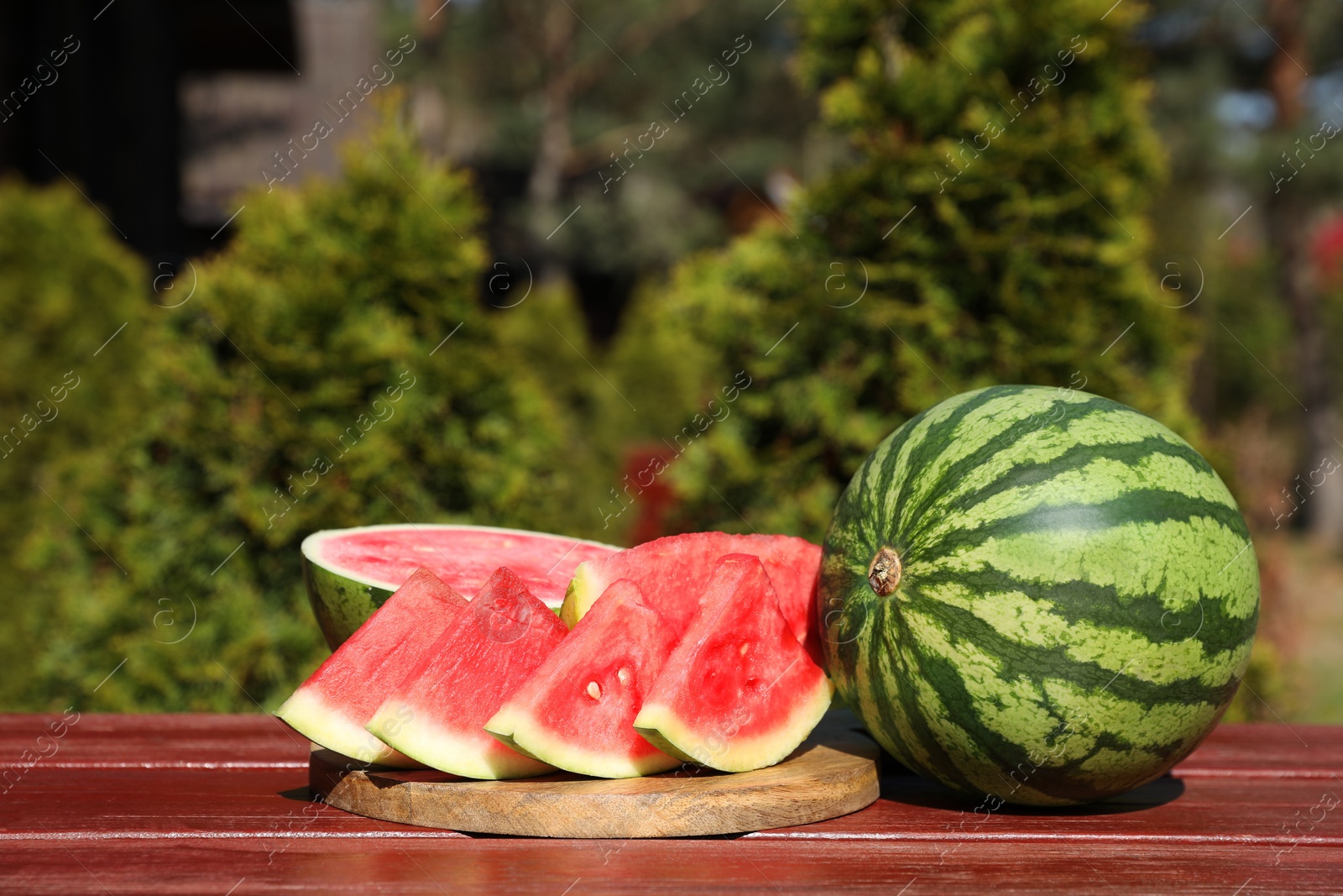 Photo of Delicious cut and whole ripe watermelons on wooden table outdoors