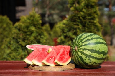 Delicious cut and whole ripe watermelons on wooden table outdoors