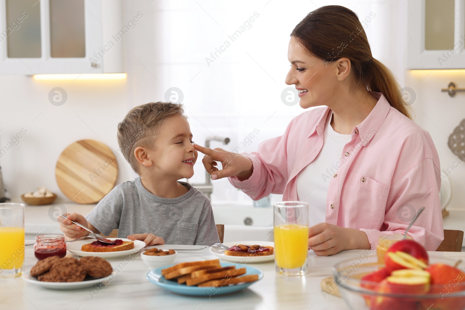 Photo of Mother and her cute little son having breakfast at table in kitchen