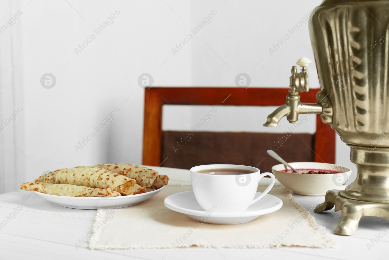 Photo of Vintage samovar, cup of hot drink and snacks served on white wooden table. Traditional Russian tea ceremony