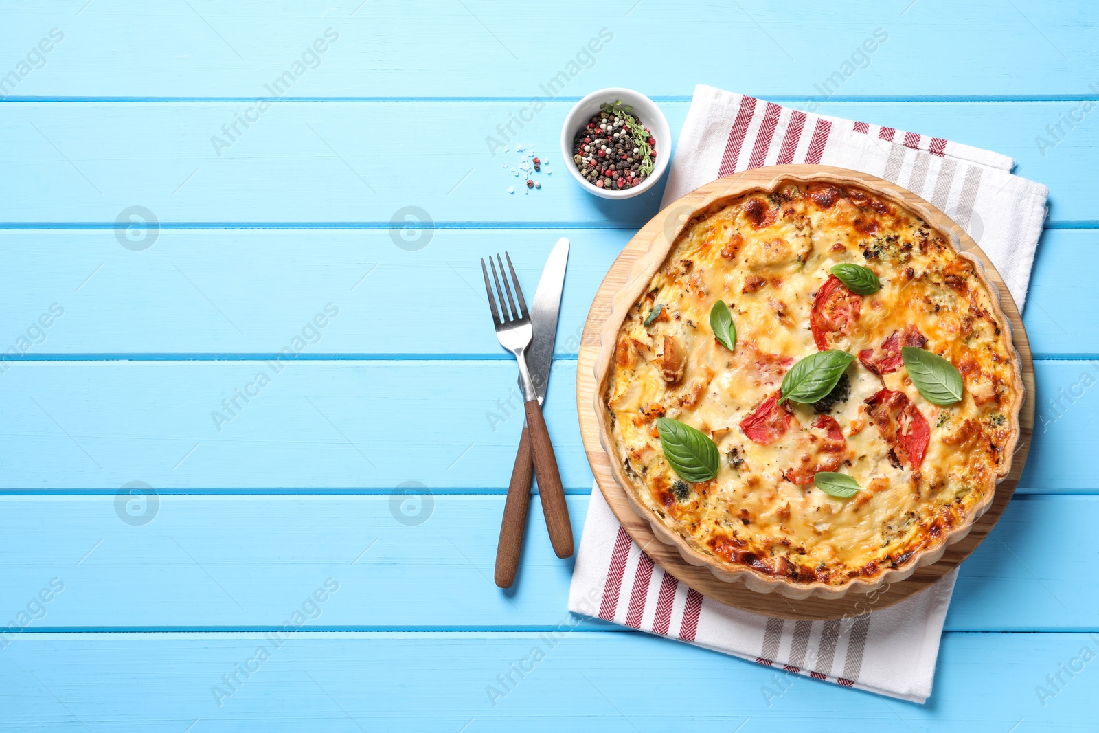 Photo of Tasty quiche with tomatoes, basil and cheese served on light blue wooden table, flat lay. Space for text