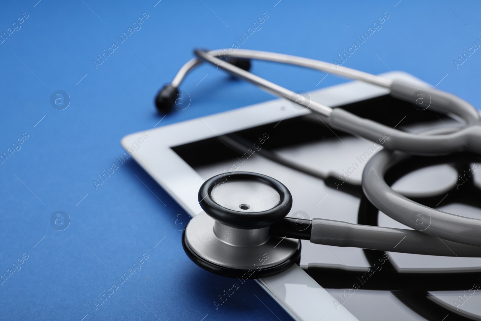 Photo of Computer tablet with stethoscope on blue background, closeup