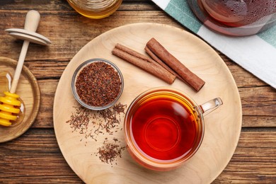 Freshly brewed rooibos tea, dry leaves and cinnamon sticks on wooden table, flat lay