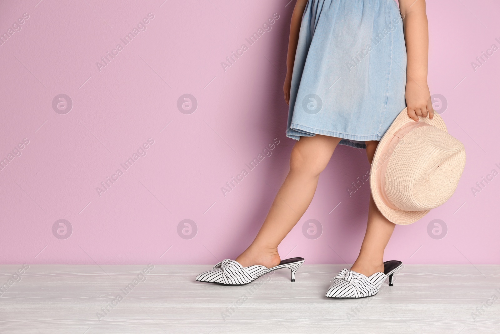 Photo of Little girl in oversized shoes near color wall with space for text, closeup on legs