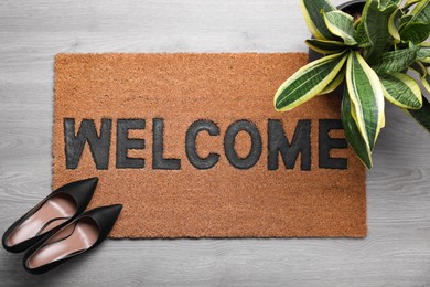 Photo of New clean mat with word WELCOME, shoes and plant on floor, top view