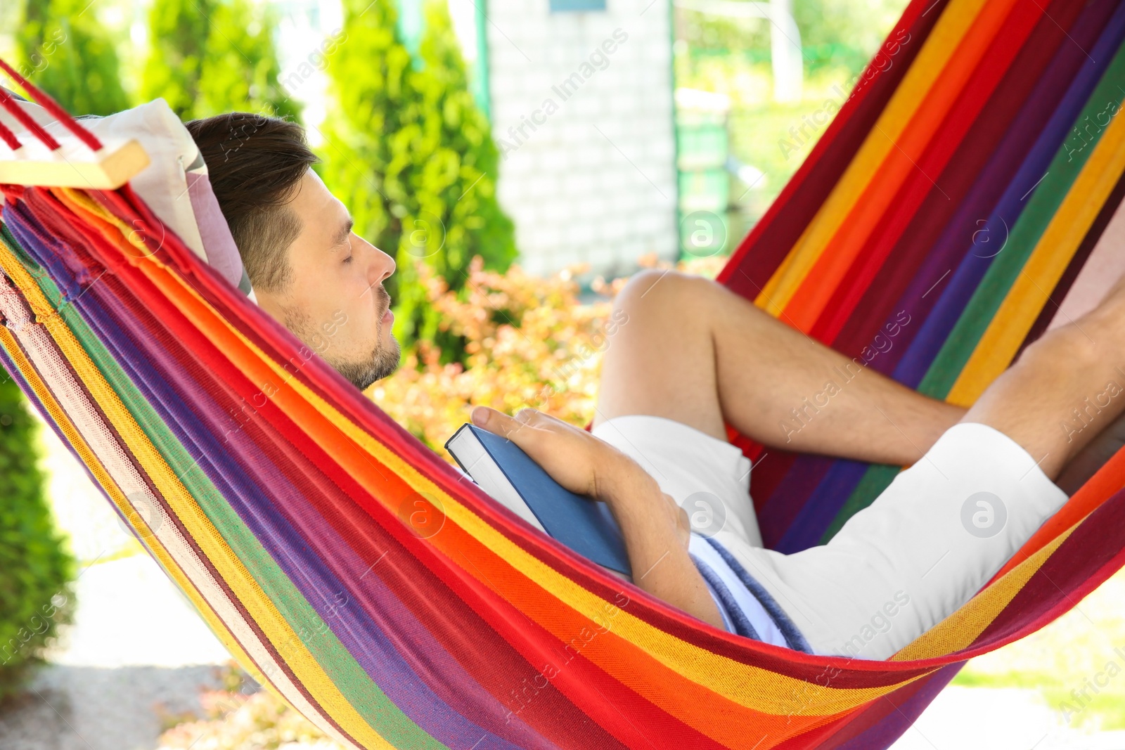Photo of Man with book sleeping in hammock outdoors on warm summer day