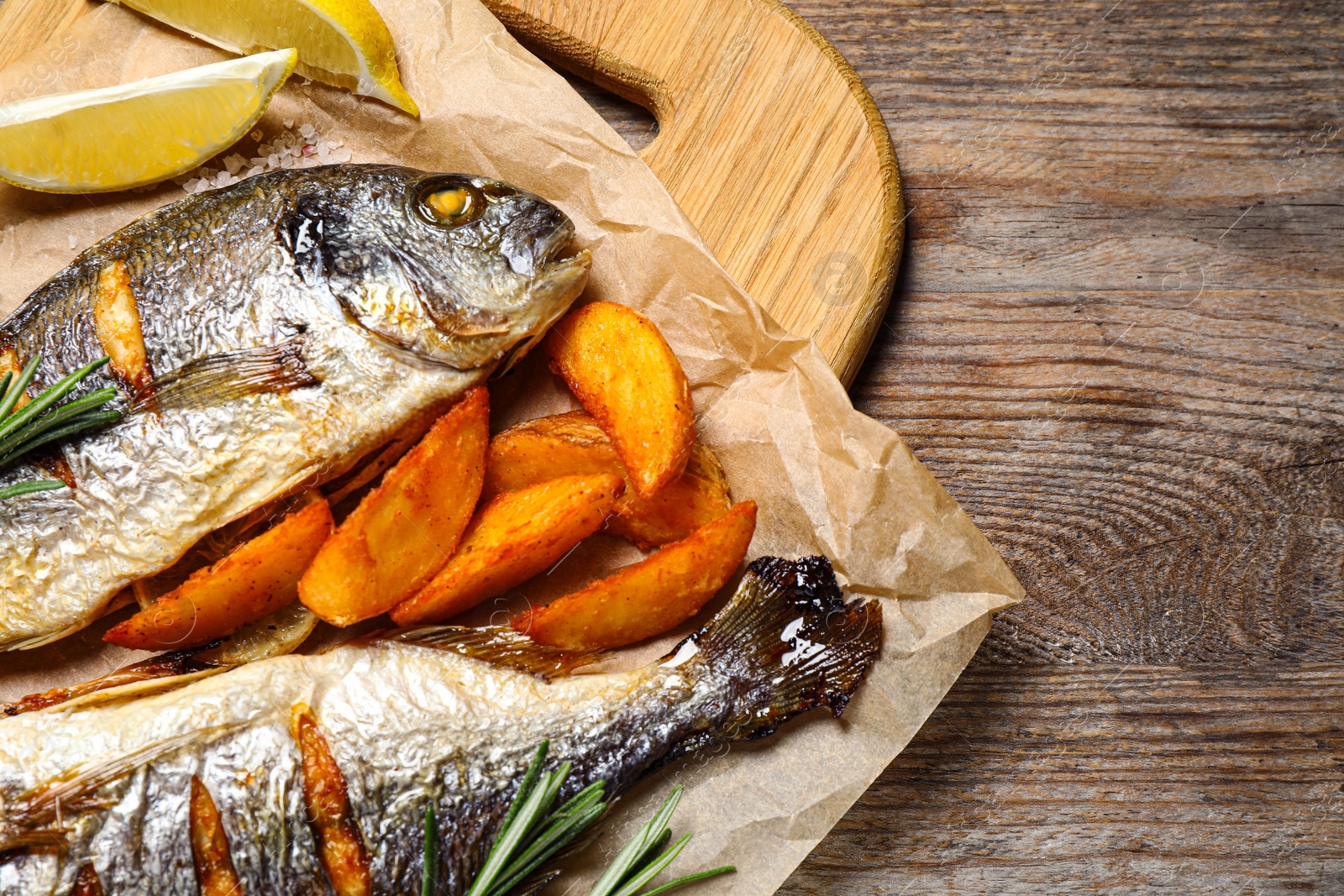 Photo of Delicious roasted fish and potatoes on wooden table, flat lay