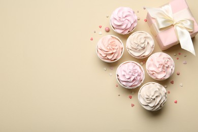 Photo of Delicious birthday cupcakes, gift box and sprinkles on beige background, flat lay. Space for text