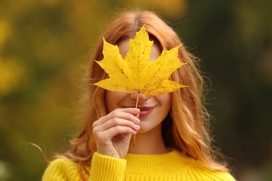 Photo of Woman covering face with autumn leaf outdoors
