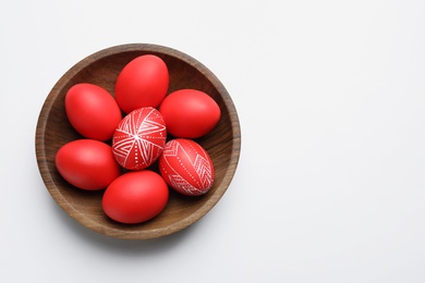 Photo of Wooden bowl with painted red Easter eggs on white background, top view