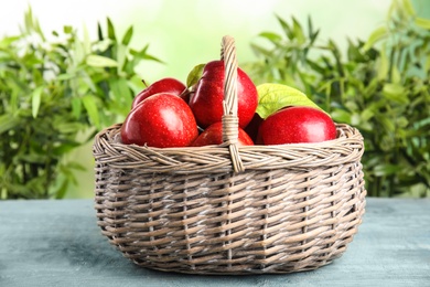 Photo of Wicker basket with ripe juicy red apples on blue table against blurred background