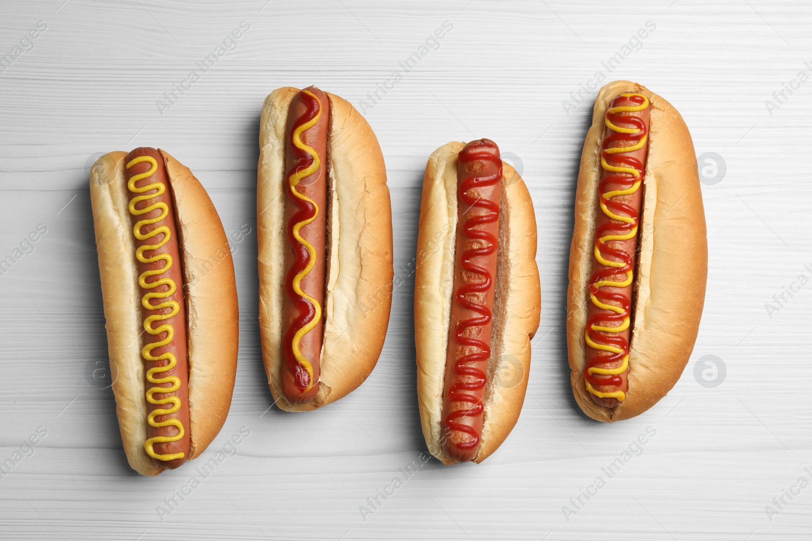 Photo of Fresh delicious hot dogs with sauces on white wooden table, flat lay