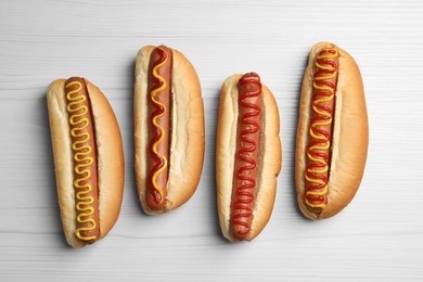Photo of Fresh delicious hot dogs with sauces on white wooden table, flat lay