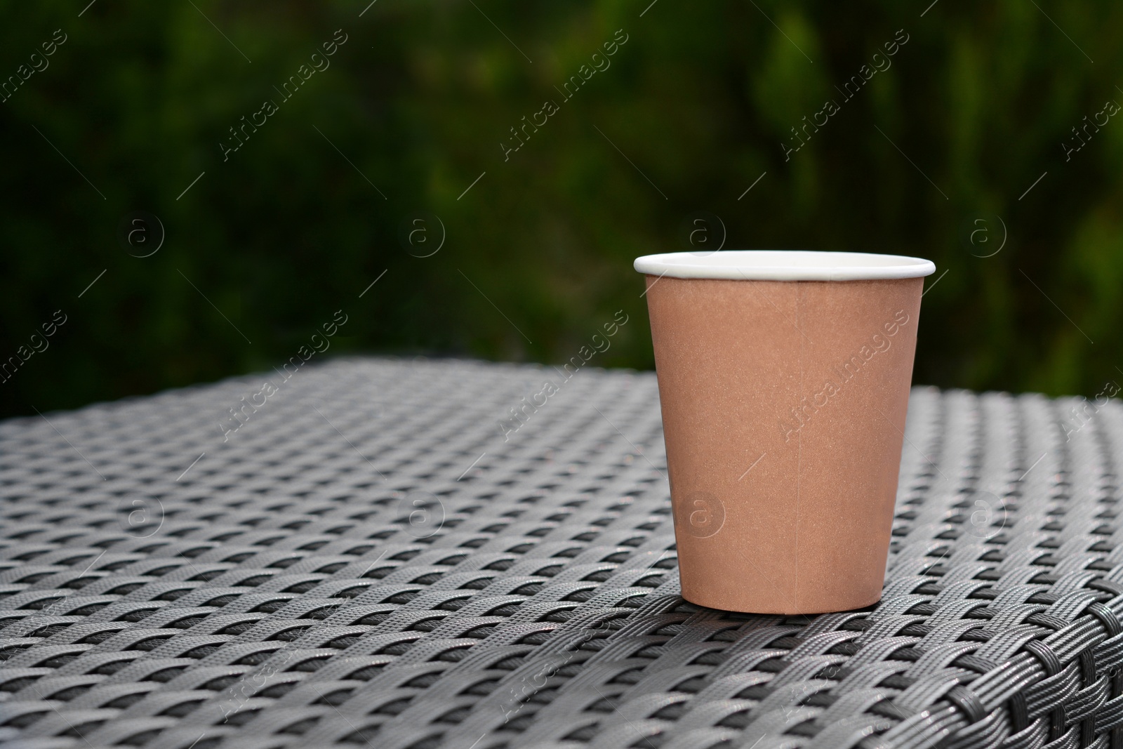 Photo of Coffee cardboard cup on rattan table outdoors, space for text