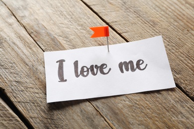 Piece of paper with phrase I Love Me on wooden table