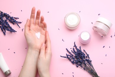 Photo of Woman applying hand cream and lavender flowers on pink background, top view