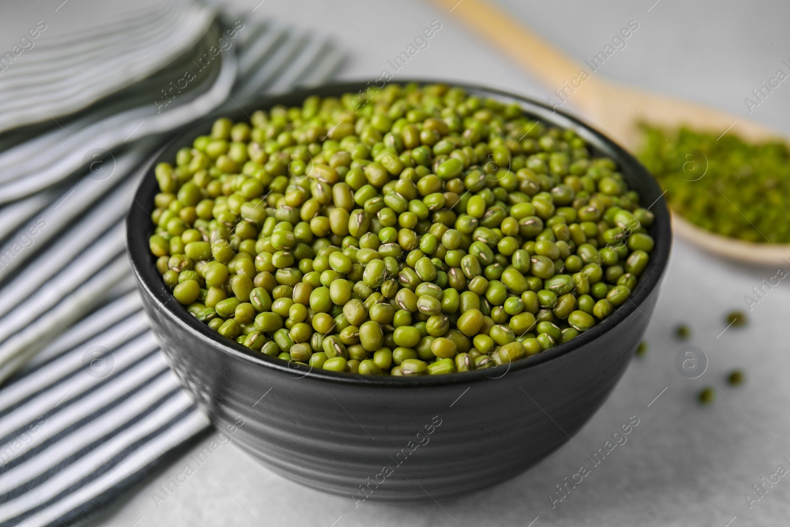 Photo of Bowl with green mung beans on grey table, closeup