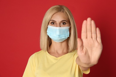 Photo of Woman in protective mask showing stop gesture on red background. Prevent spreading of coronavirus
