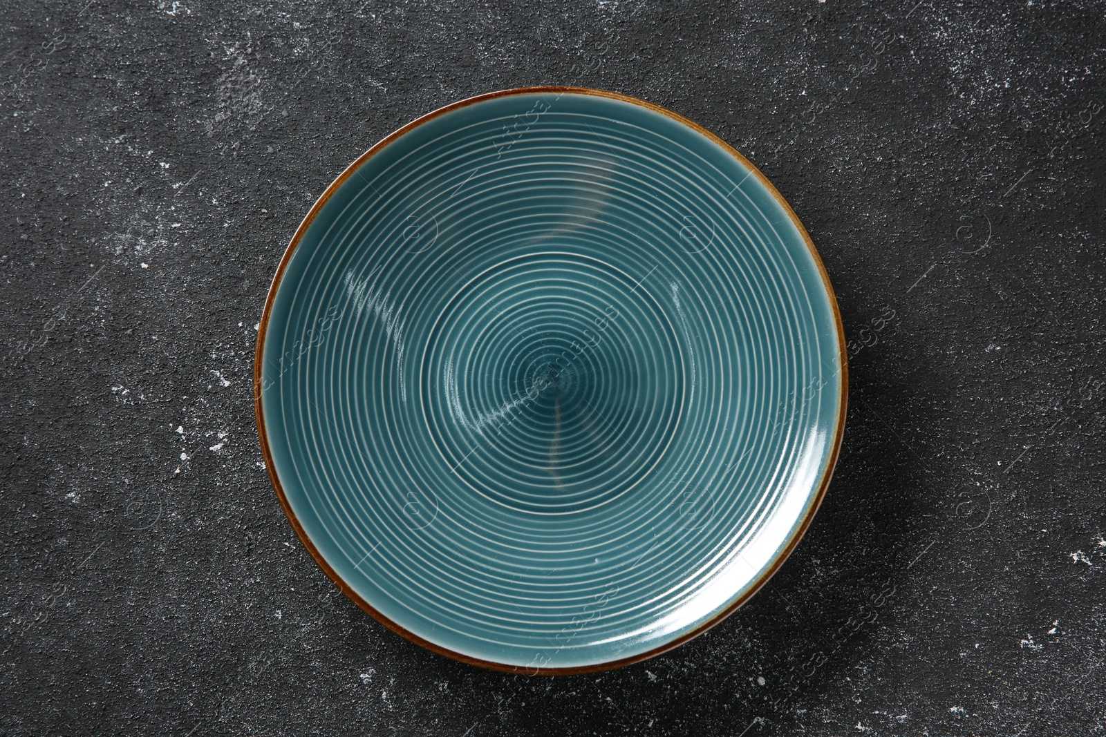 Photo of One ceramic plate on black textured table, top view