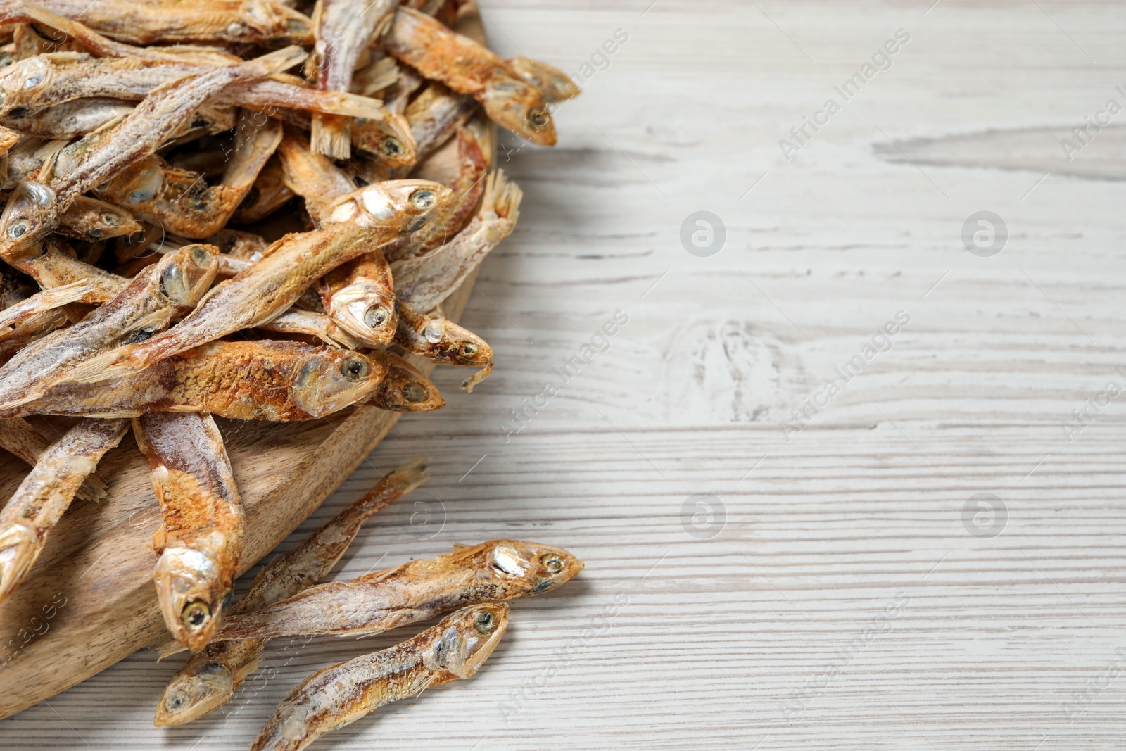 Photo of Plate of tasty dried anchovies on white wooden table, closeup. Space for text