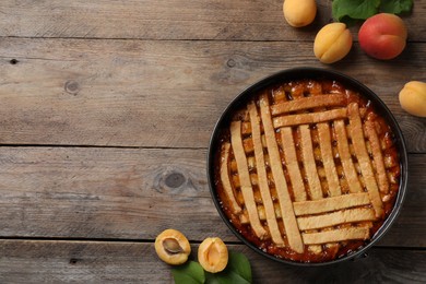 Photo of Delicious apricot pie in baking dish and fresh fruits on wooden table, flat lay. Space for text
