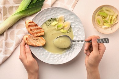 Woman eating delicious leek soup with croutons at light table, top view