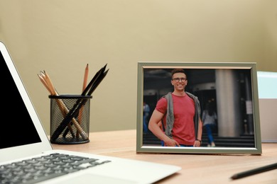 Framed photo of happy young man near laptop on wooden table in office