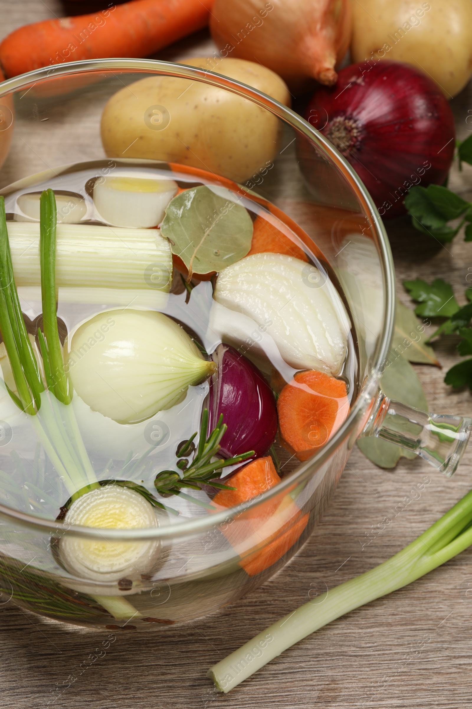 Photo of Glass pot with tasty bouillon and different ingredients on wooden table, above view