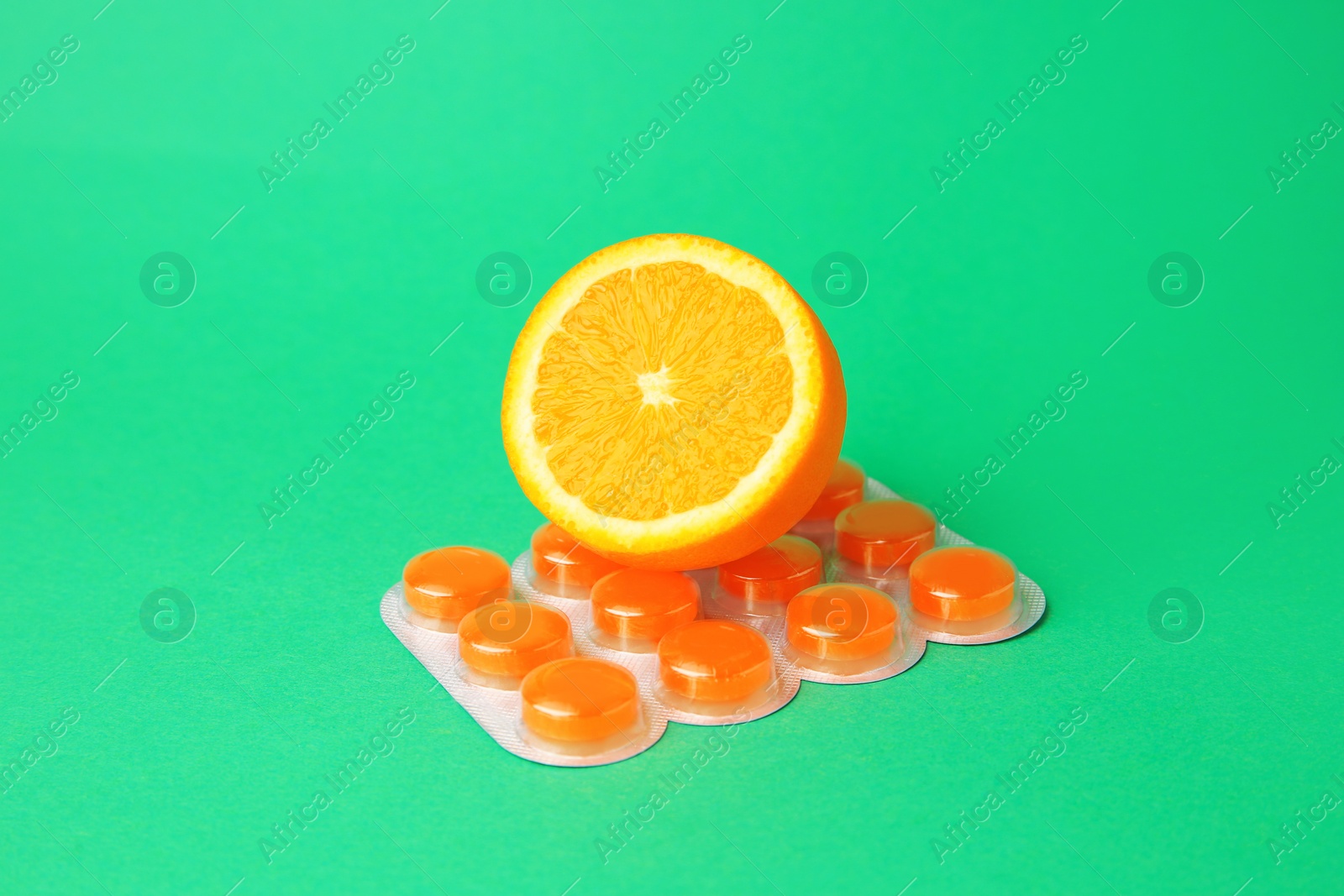 Photo of Blister with cough drops and fresh orange on green background