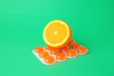 Photo of Blister with cough drops and fresh orange on green background
