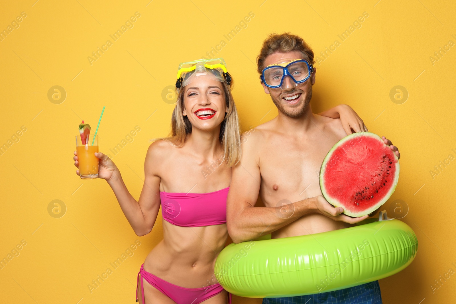 Photo of Happy young couple in beachwear with inflatable ring and cocktail on color background