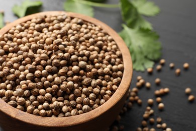 Dried coriander seeds in bowl on dark gray table, closeup