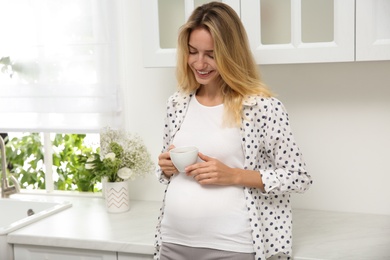 Beautiful pregnant woman drinking tea in kitchen