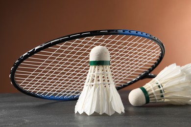 Feather badminton shuttlecocks and racket on grey table against brown background, closeup