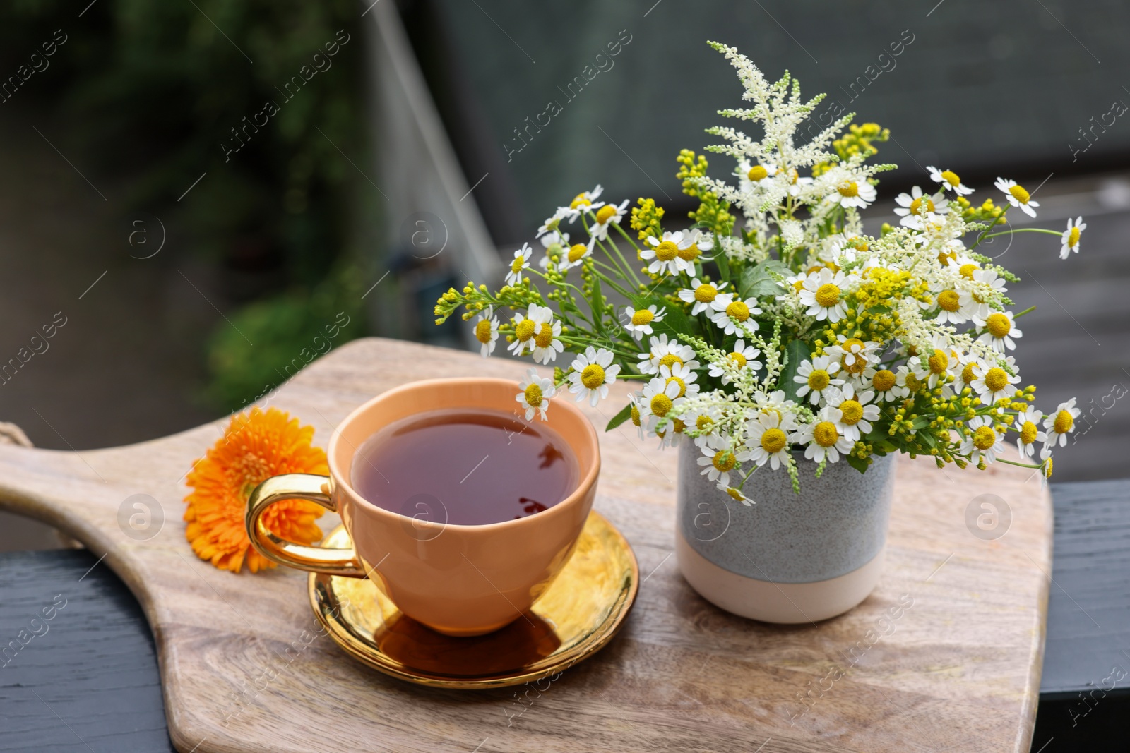 Photo of Cup of delicious chamomile tea and fresh flowers outdoors