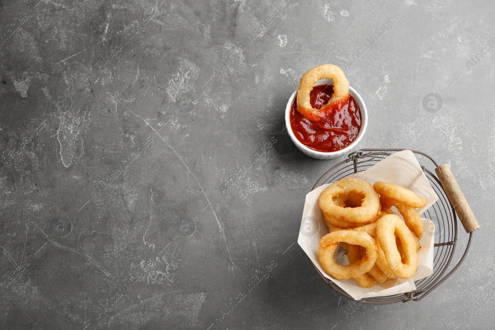 Photo of Basket with tasty onion rings and bowl of sauce on table