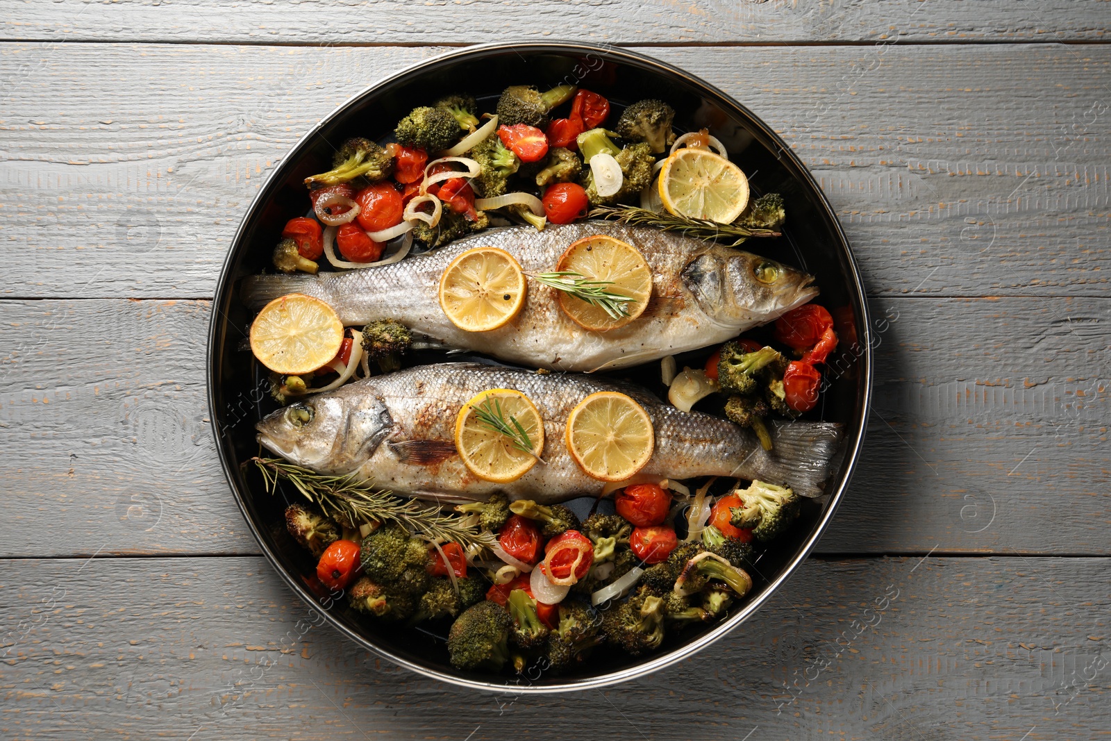 Photo of Baked fish with vegetables, rosemary and lemon on grey wooden table, top view