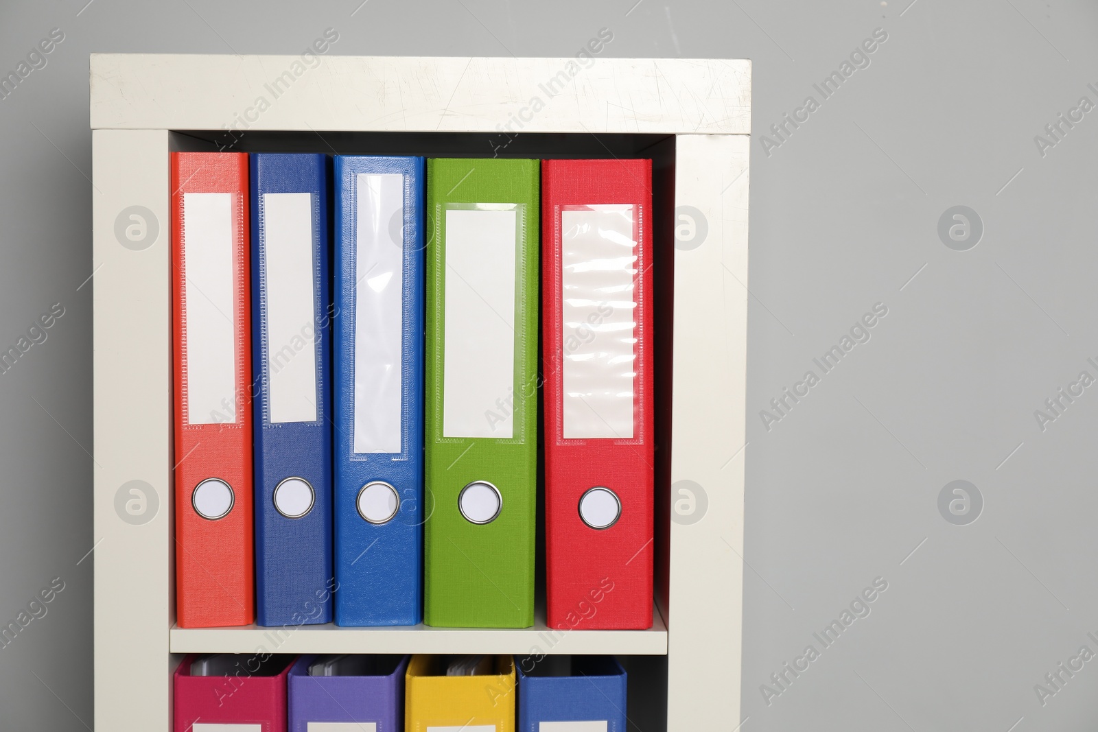 Photo of Colorful binder office folders on shelving unit near light grey wall. Space for text