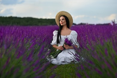 Photo of Beautiful young woman with bouquet sitting in lavender field